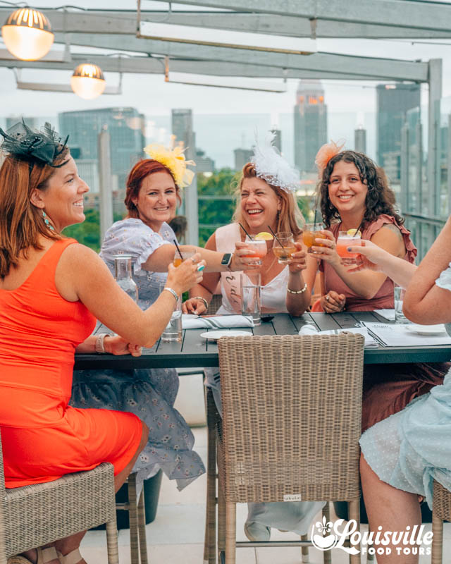 Bachelorette Party in Louisville, KY doing a cheers in front of the skyline on a rooftop bar